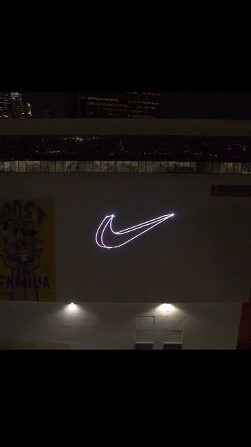 Concept demo: the Nike swoosh projected in light on a building facade at night.