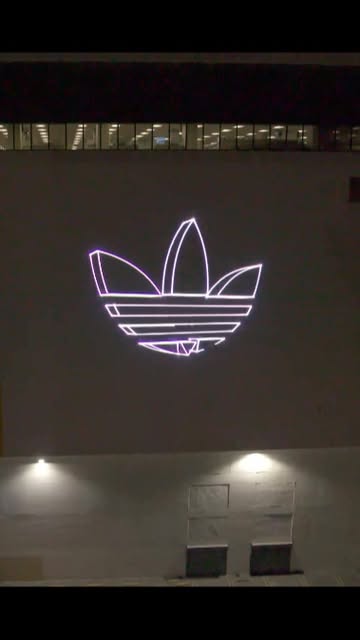 Concept demo: the Adidas trefoil projected in light on a building facade at night.
